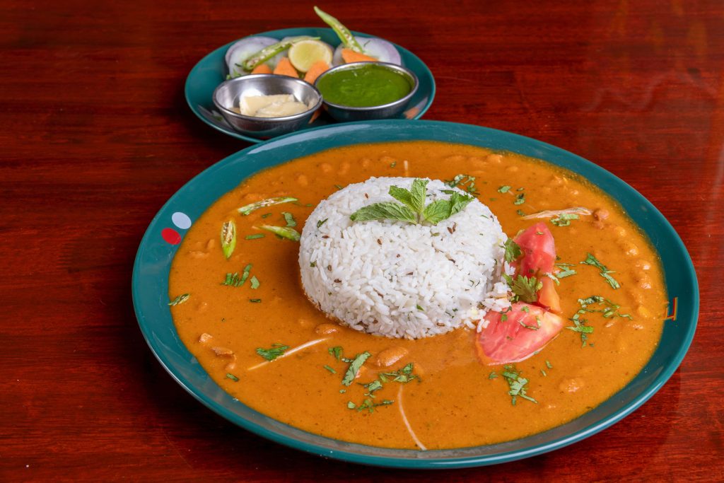 A bowl of rice and rajma curry served with a side of chutneys and onions